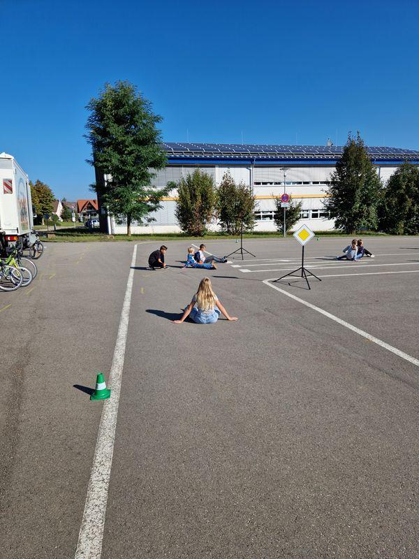 Kinder sitzen auf dem Boden des Übungsparkurs zur Fahrradprüfung
