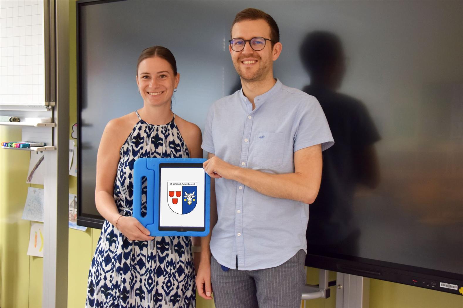 Rektorin  und ein junger Mann halten ein blaues Tablet für Kinder in der Hand