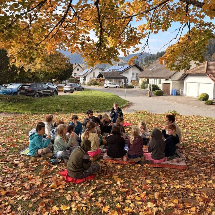 Kinder sitzen unter einem Baum auf dem laubbedeckten Boden