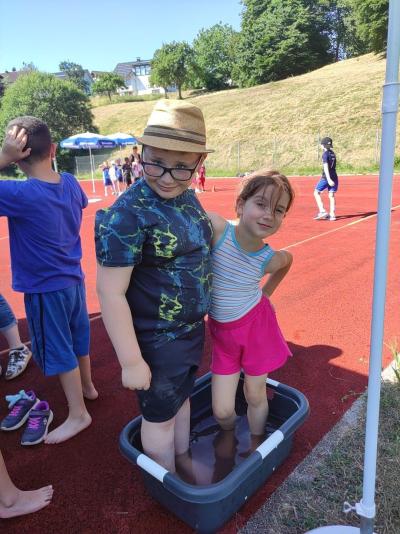 Mehrere Kinder spielen auf einer roten Sportbahn vor einem grünen Hügel.