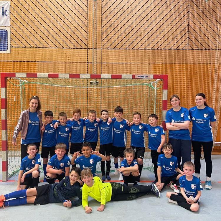 Jungenfußballmannschaft mit zwei Trainerinnen posiert vor einem Handballtor in einer Sporthalle