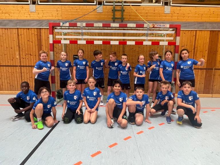 Kinder in blauen Trikots posieren in einer Sporthalle vor einem Handballtor für ein Gruppenfoto.